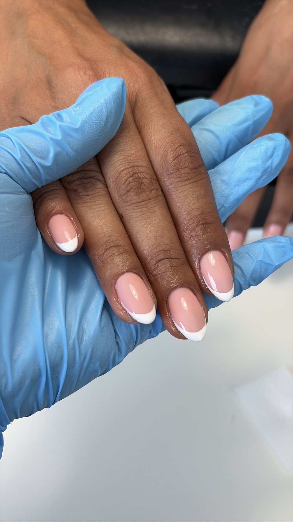 French manicure op amandelvormige nagels, de hand rust op een blauwe handschoen