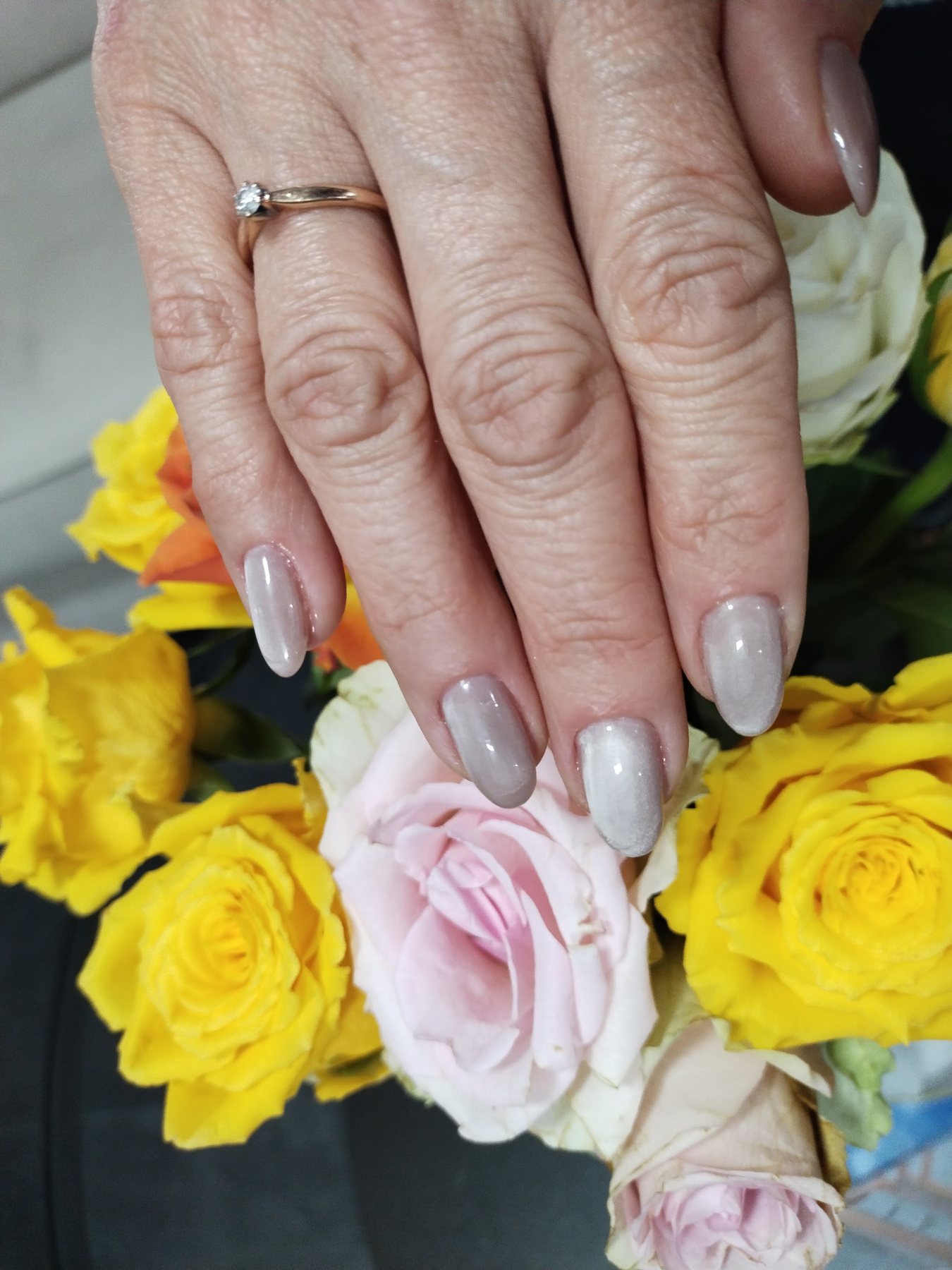 Grijs gelakte nagels boven een bos gele en roze rozen